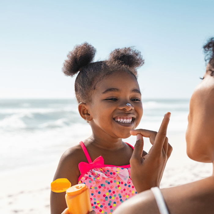 Image of mother applying suncream to smiling daughter