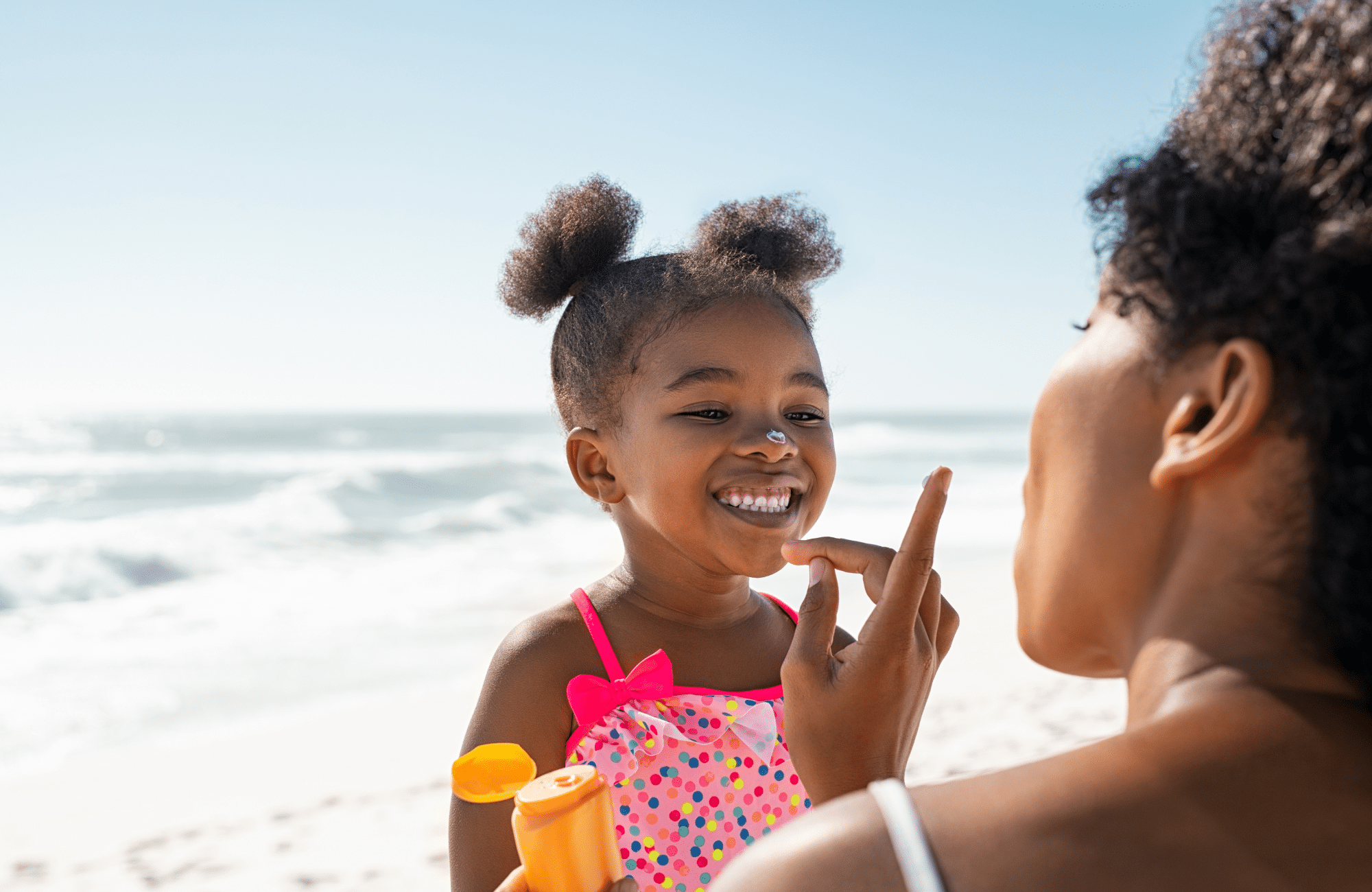 Image of mother applying suncream to smiling daughter